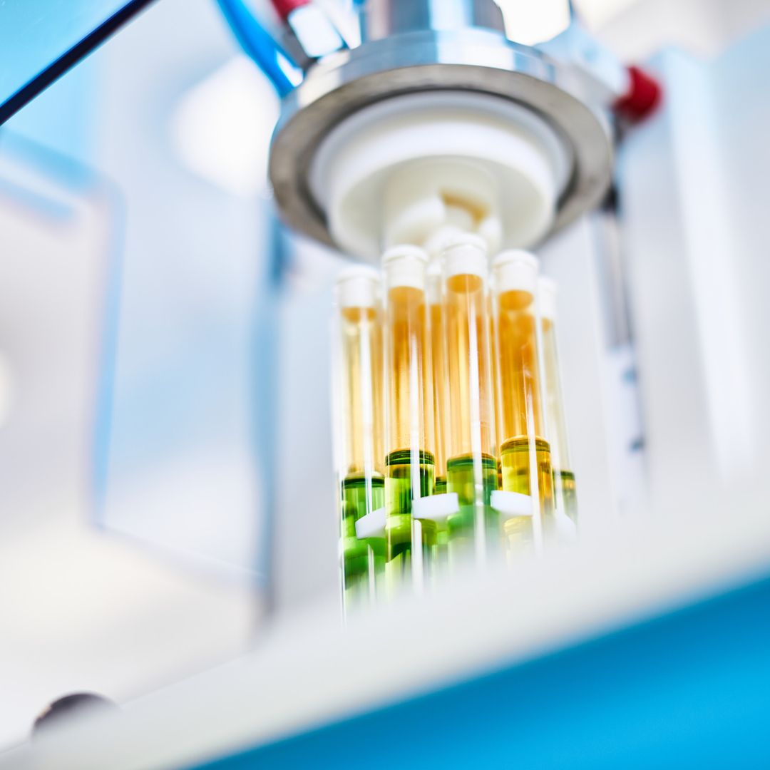 Nahaufnahme von Reagenzgläsern in einem Labor, die verschiedene farbige Flüssigkeiten, darunter grün und gelb, in einem wissenschaftlichen Instrument enthalten.