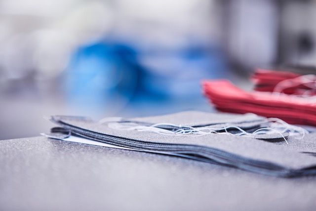 Nahaufnahme von ordentlich gestapelten Stoffmustern in Blau- und Rottönen, mit losen Fäden, die auf einer strukturierten Arbeitsfläche liegen.