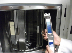 Eine Hand hält eine Farbmesskarte neben einer Metallanalysekammer, die einen präzisen Farbabgleich oder eine Prüfung in einer Laborumgebung anzeigt.