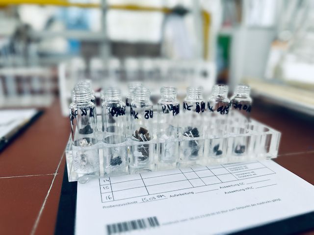 Auf einem Labortisch sind Reagenzgläser mit verschiedenen Proben und ein Datenblatt für die Probenanalyse angeordnet.