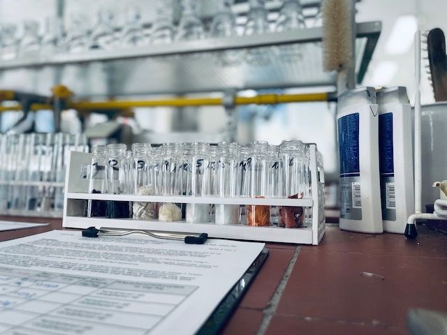 Ein Labortisch mit einem Regal mit Reagenzgläsern, die mit verschiedenen Substanzen gefüllt sind, und einem geordneten Blatt Papierkram daneben.