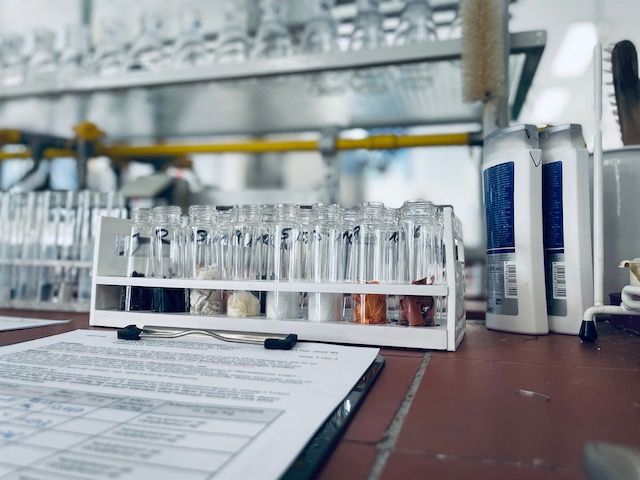 Ein Labortisch mit einem Regal mit Reagenzgläsern, die mit verschiedenen Substanzen gefüllt sind, und einem geordneten Blatt Papierkram daneben.