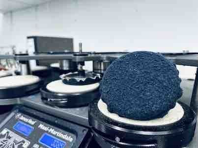 Eine blaue, strukturierte Materialprobe, die in einer Laborumgebung auf einer Heizplatte platziert und von weißen Schaumstoffkissen umgeben ist.