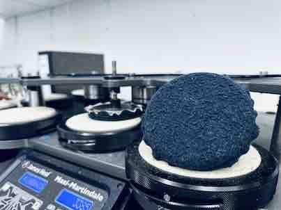 Eine blaue, strukturierte Materialprobe, die in einer Laborumgebung auf einer Heizplatte platziert und von weißen Schaumstoffkissen umgeben ist.