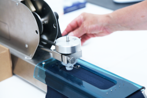 Eine Hand justiert ein präzises Messgerät an einer Stoffschneidemaschine, die eine Textilverarbeitungsanlage im Einsatz zeigt.